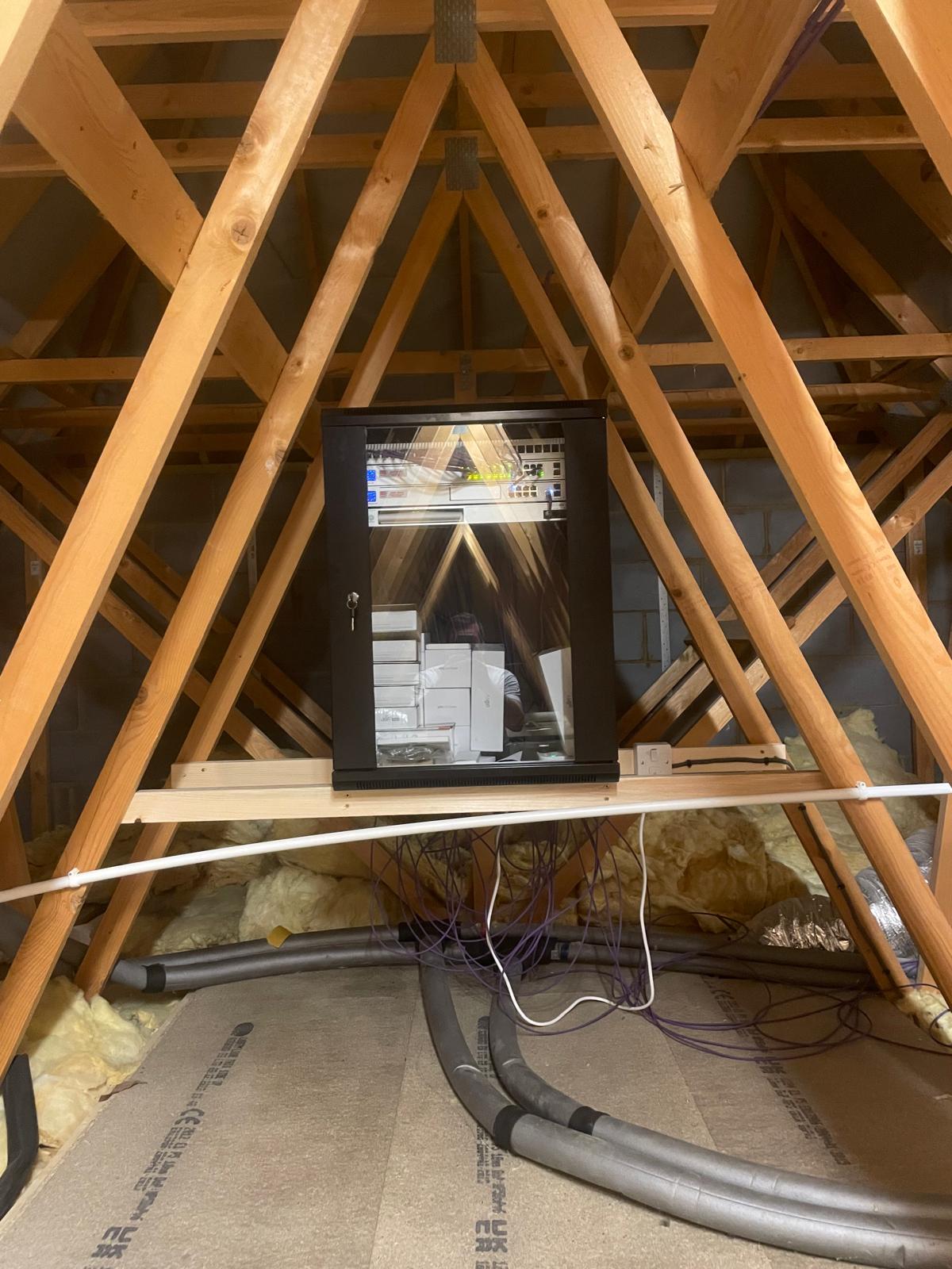 Wall-mounted network rack installed in a roof space, with UniFi networking equipment and tidy cable management